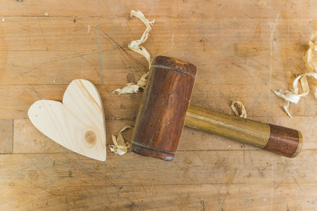 Wooden heart and a hammer with wood shavings scattered on a table in a workshop. High quality photoの写真素材