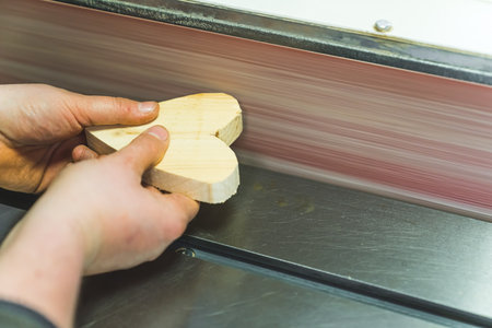 Hands of carpenter shaping edges of wooden heart using grinding machine closeup. High quality photoの写真素材