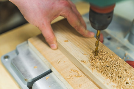 Carpenter adjusts drill bit of a professional drill machine in woodworking space. High quality photo