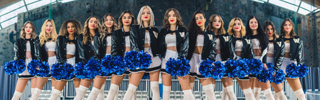 Wide shot of cheerleader female team in black and white uniform posing for a camera. High quality...