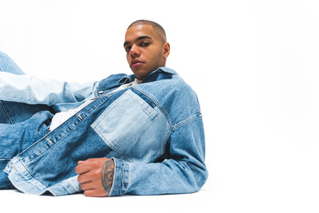 African American man with serious facial expression wearing denim jacket and jeans posing on the floor against a white background. High quality 4k footageの写真素材