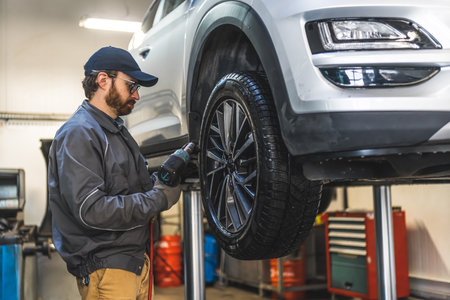 Car mechanic replacing wheel of a lifted vehicle with pneumatic wrench in garage of repair service station. High quality photoの写真素材