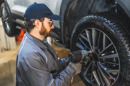 Mechanic with electric drill changing car tire on a lifted vehicle in repair shop. High quality photoの写真素材