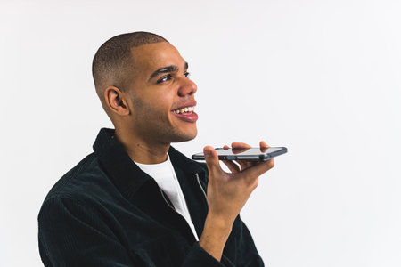 Black man talking on call holding smartphone near his mouth using speakerphone. Smart voice application. High quality photoの写真素材