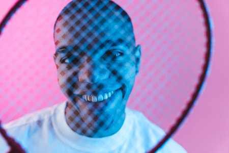 Cheerful black young man looking through the badminton racket net sports concept. High quality photoの写真素材