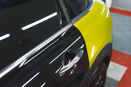 Car wrapping concept. Closeup shot of special vinyl film in lime yellow glued onto the surface of modern black car. High quality photoの写真素材