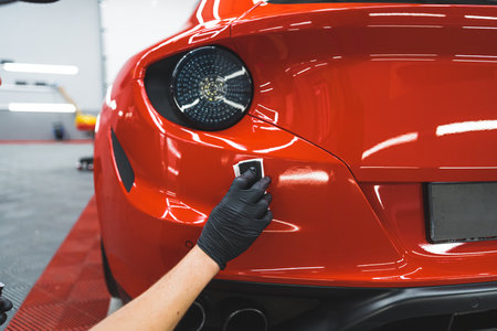 Car detailing process. Beautiful red sports cars paint being wrapped with transparent vehicle vinyl foil. Back indoor shot. High quality photoの写真素材