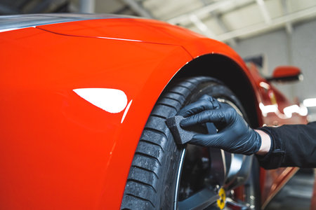 Closeup shot of blackening tires car detailing of a red sports car. Car detailing process. Cleaning tires with a sponge. High quality photoの写真素材