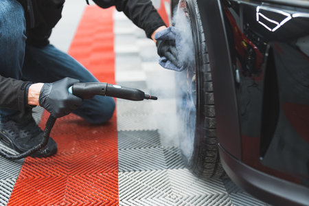 Low angle view of a hot steam machine used for deep cleaning of wheels and tires during car detailing process. Black car. High quality photoの写真素材