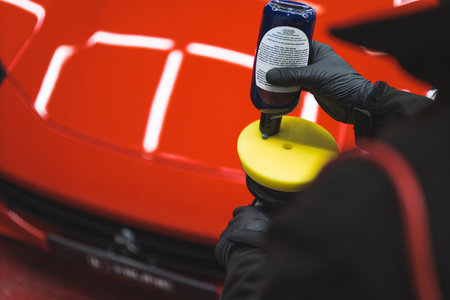 Applying polish on car. High angle closeup shot of professional car detailing worker distributing polishing product onto orbital car polish. High quality photoの写真素材