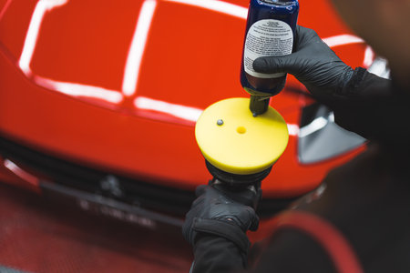 Polishing product distributed onto orbital polisher. Closeup shot with blurred red sports car in the background. High quality photoの写真素材