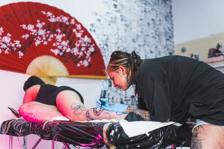 a customer laying on a bed and a tattoo artist applying ink on her leg, tattoo salon. High quality photoの写真素材