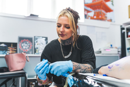 a young tattoo artist girl preparing a tattoo machine to start drawing, medium shot, tattoo salon. High quality photoの写真素材