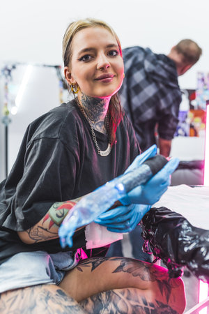 nice-looking tattooist girl working in the studio and smiling to the camera, medium vertical shot. High quality photoの写真素材