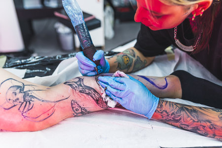 A professional tattoo artist makes a black and white tattoo on a womans leg, applying in ink. The process of tattooing the skin. High quality photoの写真素材