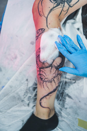 vertical shot of a tattoo artist supplying soap foam on a new-made tattoo on a leg. High quality photoの写真素材