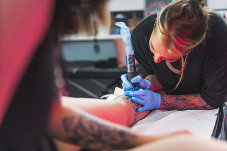 professional tattooist with special gloves drawing on a clients leg by a machine. High quality photoの写真素材