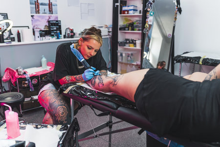 tattooed art master making a new tattoo for a customer on her leg, art studio. High quality photoの写真素材
