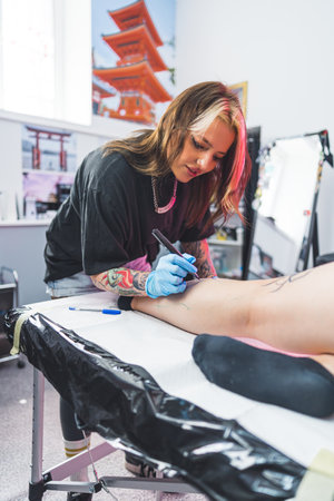 a client lying on the table and a tattoo master drawing on her leg with Freehand technique. High quality photoの写真素材