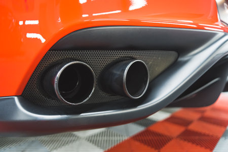 Indoor closeup shot of two exhaust pipes or tailpipes of a fast red sports car. A visit at mechanics or car detailing studio. High quality photoの写真素材