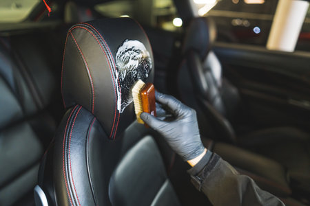 Closeup shot of interior car detailing of a leather car seat with a small brush and cleansing product. Blurred background. High quality photoの写真素材