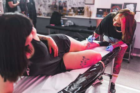 a client lying on the table and a tattooist drawing on her leg with a marker, Freehand technique. High quality photoの写真素材