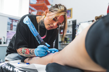 young concentrated tattoo master girl applying on a leg and drawing a new tattoo. High quality photoの写真素材
