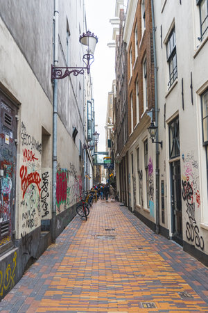 04.18.2023 Amsterdam, Netherlands. Empty Amsterdam street in between building blocks. Graffiti on the walls. Vertical shot. High quality photoのeditorial素材
