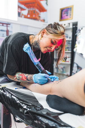 pleased tattoo artist girl applying ink on a clients leg, working in the tattoo studio. High quality photoの写真素材