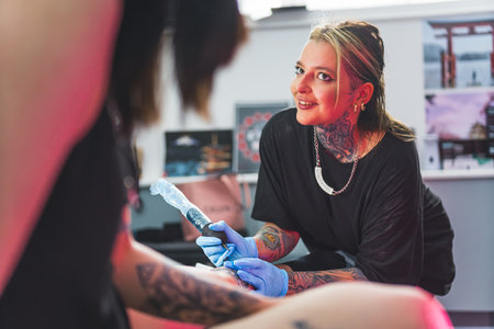 cheerful tattoo artist girl talking to her customer while drawing a tattoo in the studio. High quality photoの写真素材