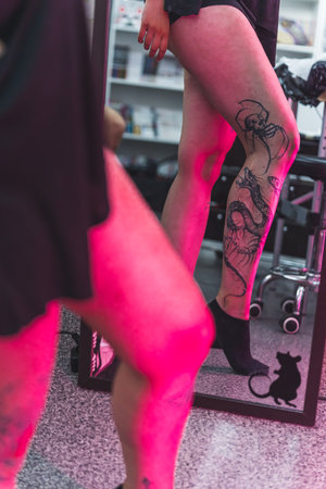 unknown woman looking at her new tattoo on her leg in the mirror, tattoo studio vertical shot. High quality photoの写真素材