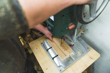 Closeup holding a wooden board and making holes in it with electric drill machine . High quality...