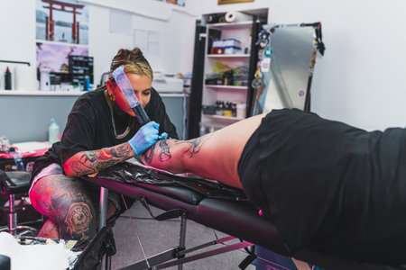 concentrated tattoo master working on a new tattoo on a leg, tattoo studio. High quality photoの写真素材