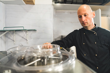 Pastry chef at work. Bald caucasian man attentively oversees the operation of professional ice cream mixer. High quality photoの写真素材