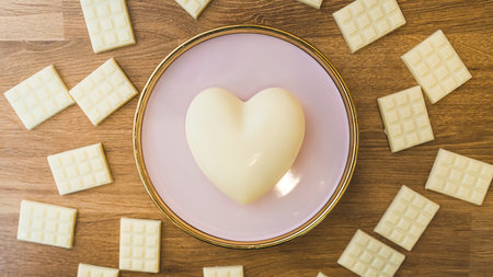Craft heart-shaped white chocolate on pink plate with bars of white chocolate on wooden table. Valentines day concept. Medium closeup indoors shot. High quality photoの写真素材