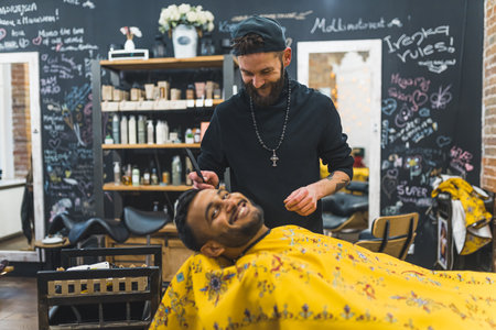 Indian client getting his facial hair trimmed by a skilled barber in a barbershop. Smiling and looking at the camera. High quality photoの写真素材