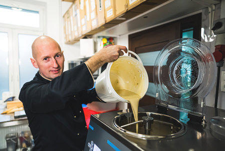 Chef pouring ice cream into ice cream into big steel ice cream machine. Production concept. Bald caucasian male chef at work making ice cream. High quality photoの写真素材