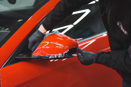 car specialist applying vinyl wrap on a mirror to protect it from painting, repair shop. High quality photoの写真素材