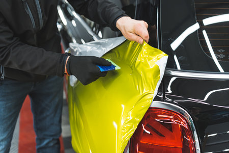 Closeup shot of car wrapping process. Two hands applying neon yellow vehicle vinyl wrap onto the surface of a black car. High quality photoの写真素材