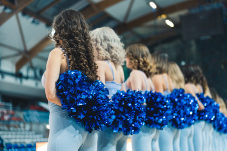 Shot from the back of women cheerleaders standing in line with blue pompons on a basketball court. High quality photoの写真素材