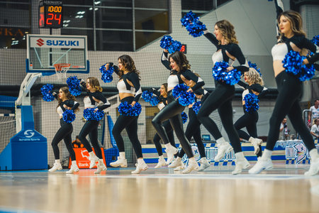 A group of young women cheerleaders dancing with pompons on a basketball court. High quality photo