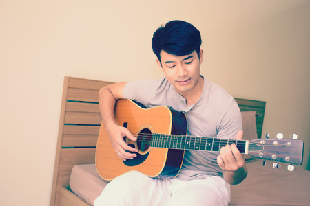 Asian young man singing and playing a guitar at room, vintage color tone.の写真素材