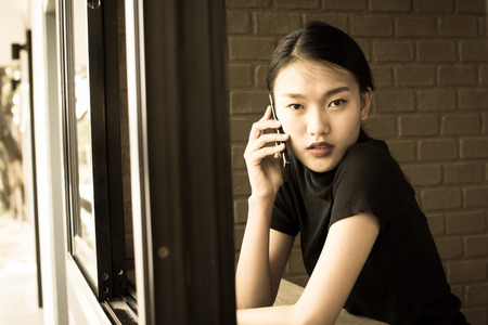 Asian young beautiful woman talking with smart phone, vintage color tone.の写真素材