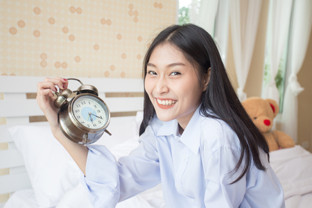 Happy young asian woman hold clock with attractive smiling, 20s year old.の写真素材