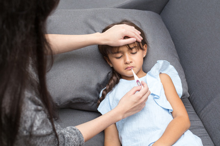 Caring mother touching head on sick daughter forehead at home.の写真素材