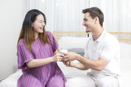 Man give milk to pregnant woman with smiling together in bedroom, man and woman with family concept, 2 person.の写真素材