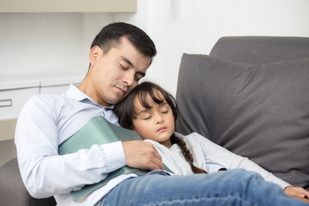 Happy father sleeping with daughter in sofa while holding book.の写真素材