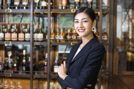 Young Asian Woman Restaurant Standing with Happy Emotion. Woman Present Wine for Customer at Bar. Woman with Wine in Bar Concept.の写真素材