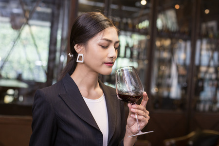Young Asian Sommelier Woman tasting Red Wine with Relax Emotion. The Woman is holding  wineglass and Smell. Woman with Sommelier and Wine Concept.の写真素材