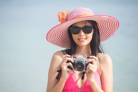 Portrait of Beautiful Asian Woman holding retro Camera at the Beach, People with Summer Concept, ...